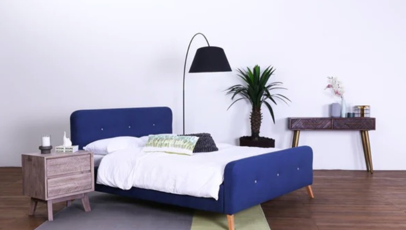 Blue bed frame upholstered in fabric with wooden legs.